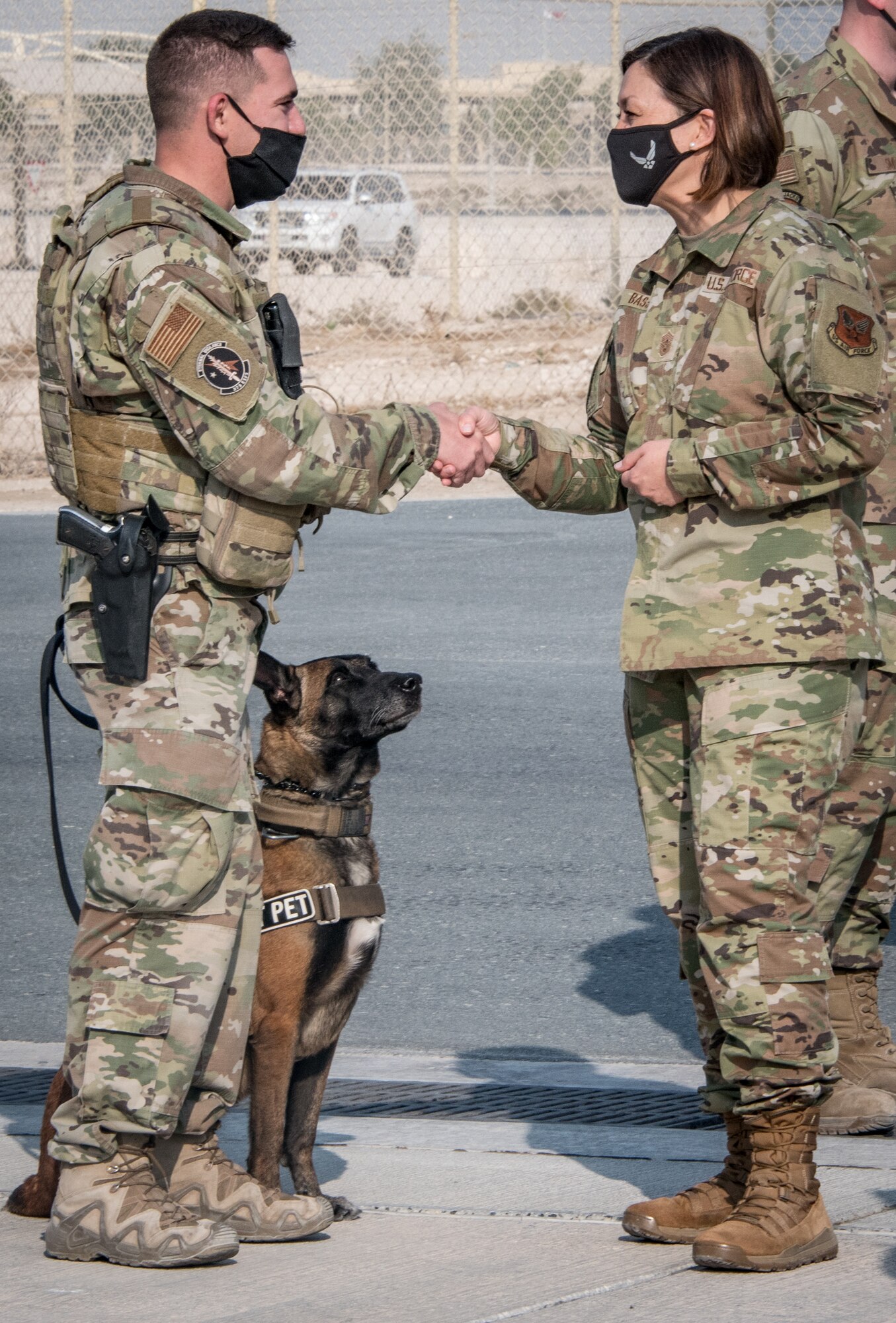 two people shake hands while a military working dog sits and observes
