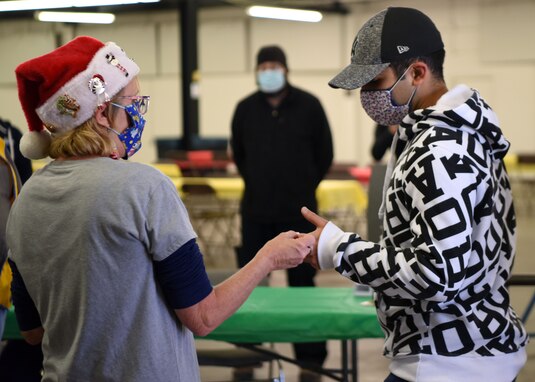 The 17th Logistics Readiness Squadron quality assurance inspector Karen Martin, hands a raffle ticket to a military member while greeting them at the Home Away From Home event in the First Financial Pavilion in San Angelo, Texas, Dec. 25, 2020. All attendees received temperature checks before admittance to ensure the safety of all personnel. (U.S. Air Force photo by Airman 1st Class Ethan Sherwood)