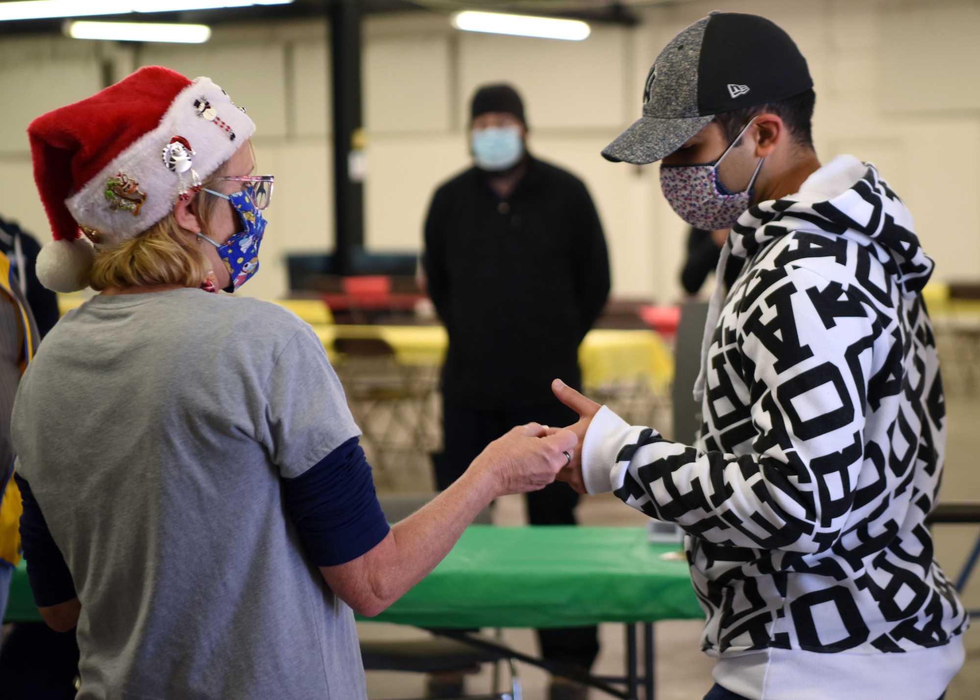 The 17th Logistics Readiness Squadron quality assurance inspector Karen Martin, hands a raffle ticket to a military member while greeting them at the Home Away From Home event in the First Financial Pavilion in San Angelo, Texas, Dec. 25, 2020. All attendees received temperature checks before admittance to ensure the safety of all personnel. (U.S. Air Force photo by Airman 1st Class Ethan Sherwood)