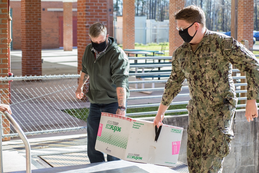 Personnel with Naval Health Clinic Cherry Point (NHCCP), North Carolina, carry in the first shipment of the Moderna COVID-19 Vaccine at Marine Corps Air Station Cherry Point, North Carolina, on Dec. 22, 2020.