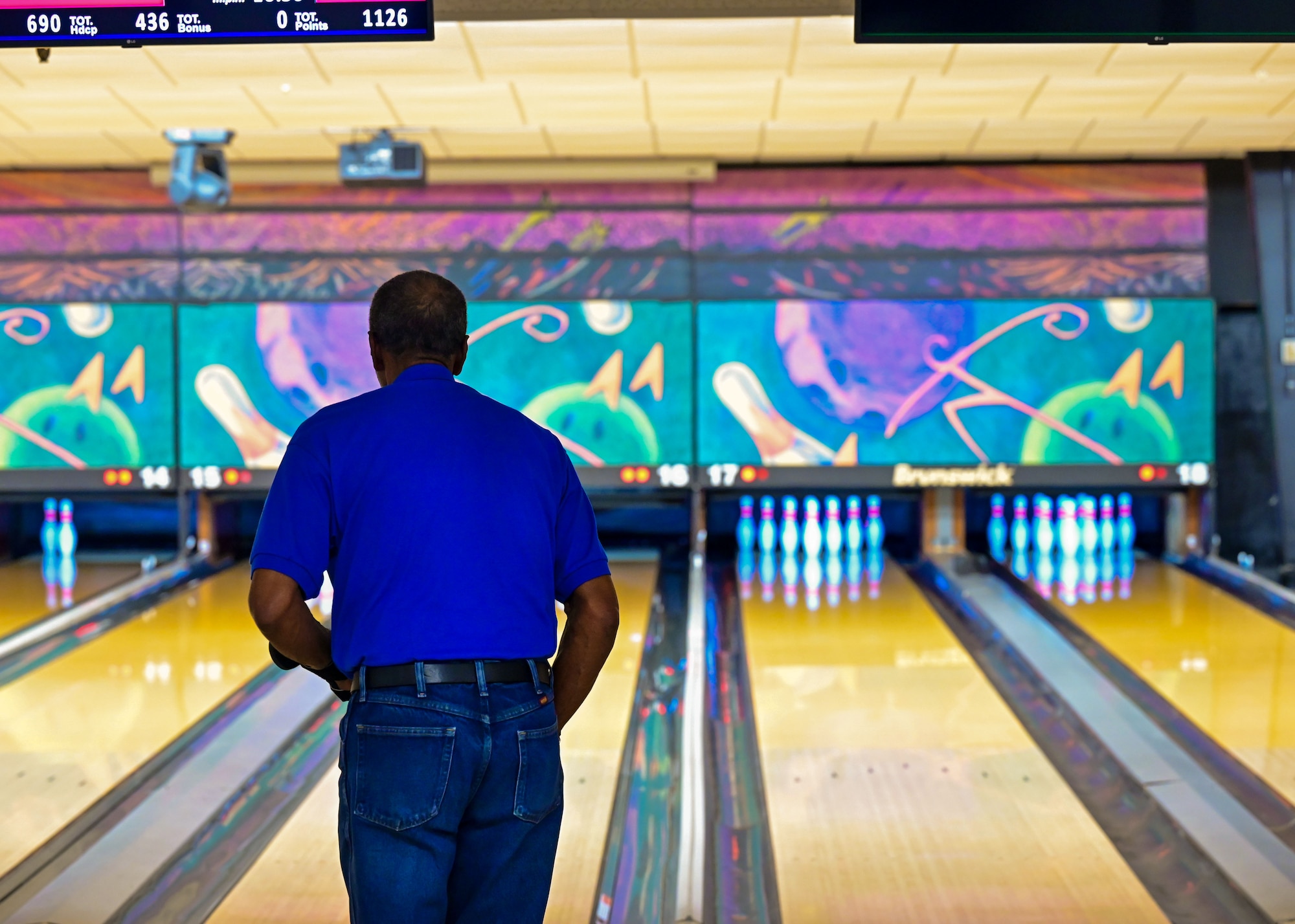 A man looks down a bowling lane as he prepares to throw a ball at the pins at the end of the lane.