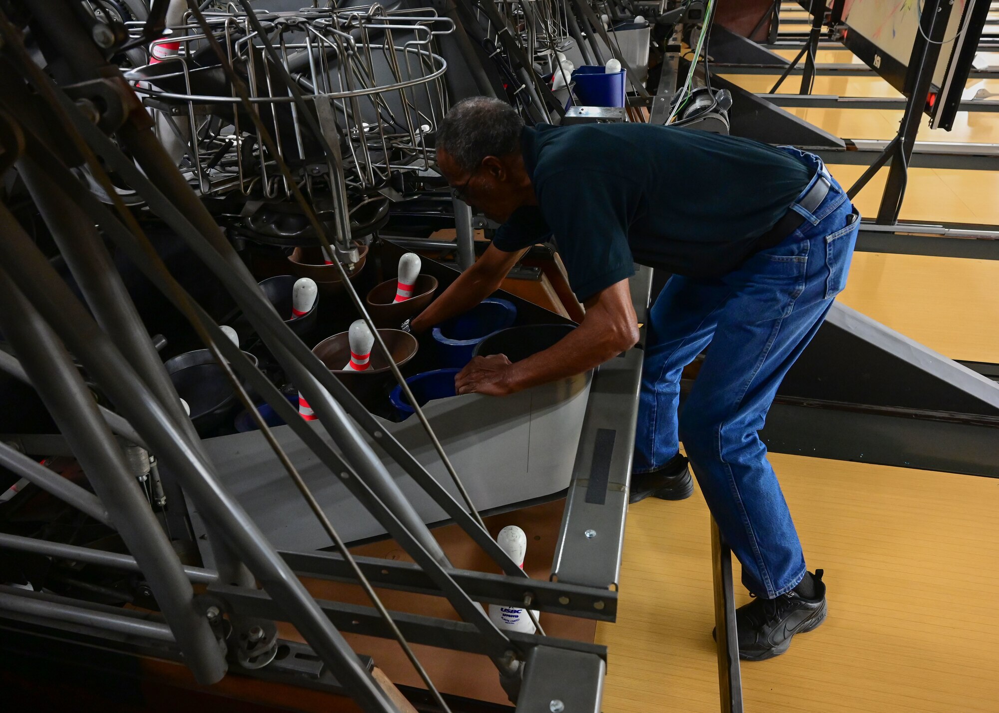 A man uses a tool to fix a pinsetter machine.
