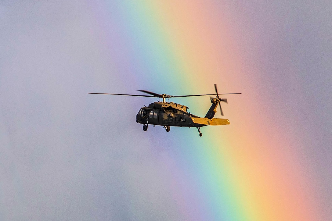 An Army helicopter flies by a rainbow.