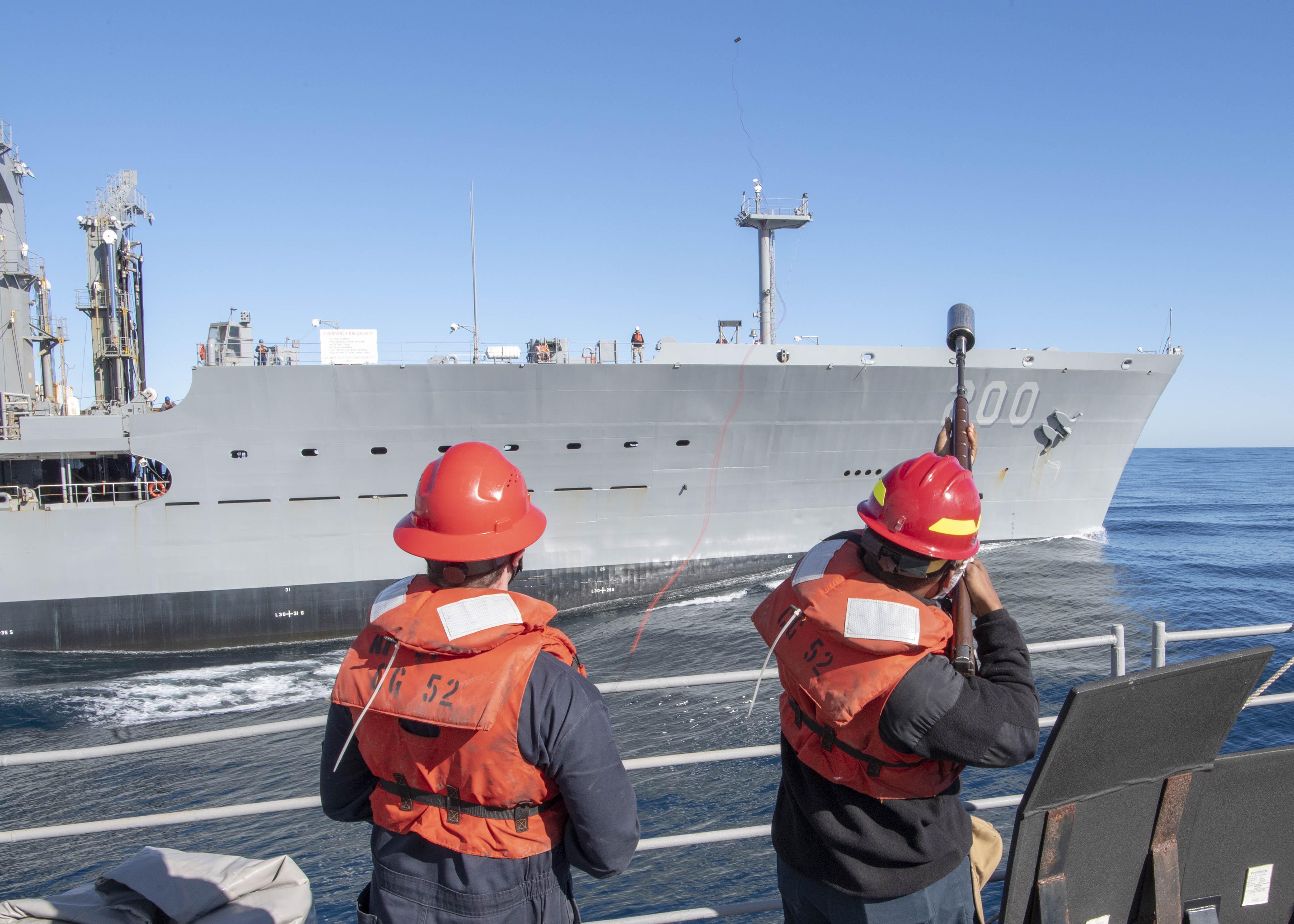 Gunner's Mate 2nd Class Shawn Trostin, from Miami, left, observes Gunner's Mate Seaman Jalen Powell, from Flint, Mich., fire a shot line from the Ticonderoga-class guided-missile cruiser USS Bunker Hill (CG 52) to the Military Sealift Command fleet replenishment oiler USNS Guadalupe (T-AO 200) during a replenishment-at-sea Dec. 19, 2020.
