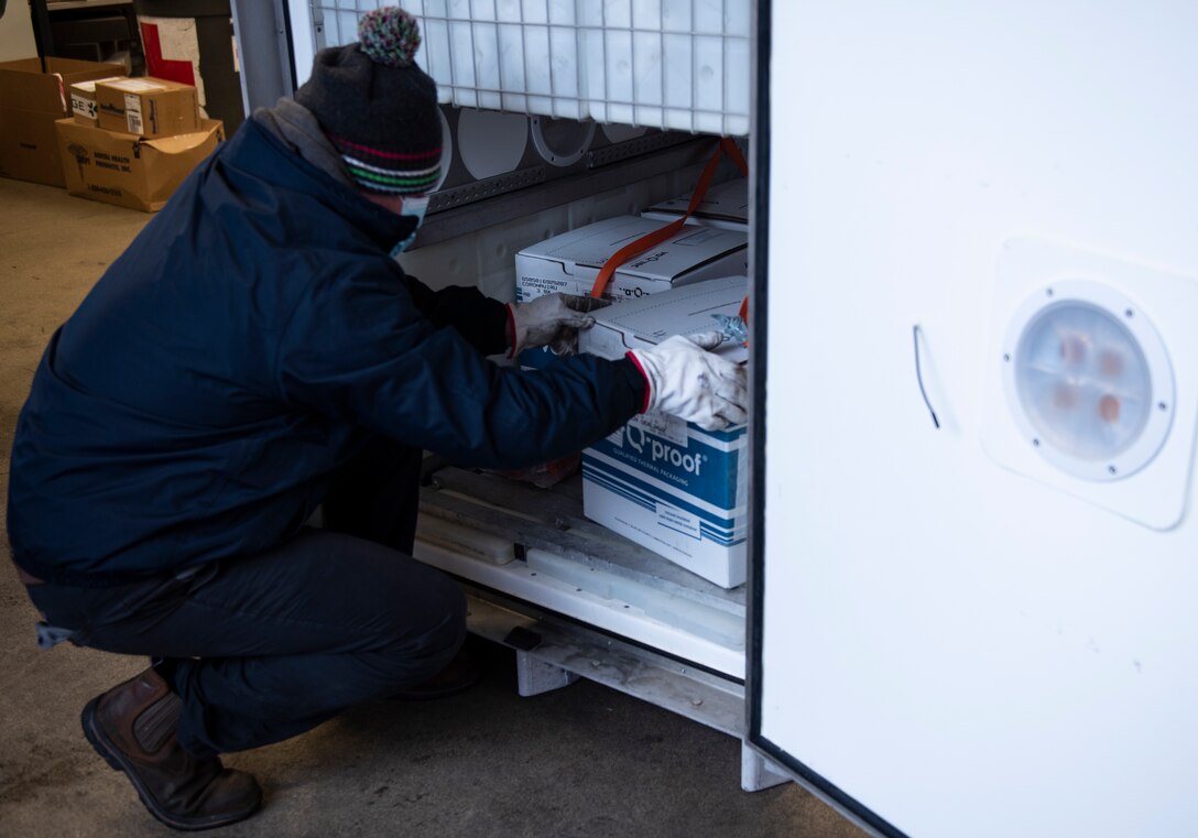 Delivery personnel removes boxes of COVID-19 vaccinations from a temperature-controlled vessel at Royal Air Force Lakenheath, England, Dec. 27, 2020. The United States Government has purchased the vaccines and is making them available to the Department of Defense for distribution and administration to DoD personnel. (U.S. Air Force photo by Airman 1st Class Jessi Monte)