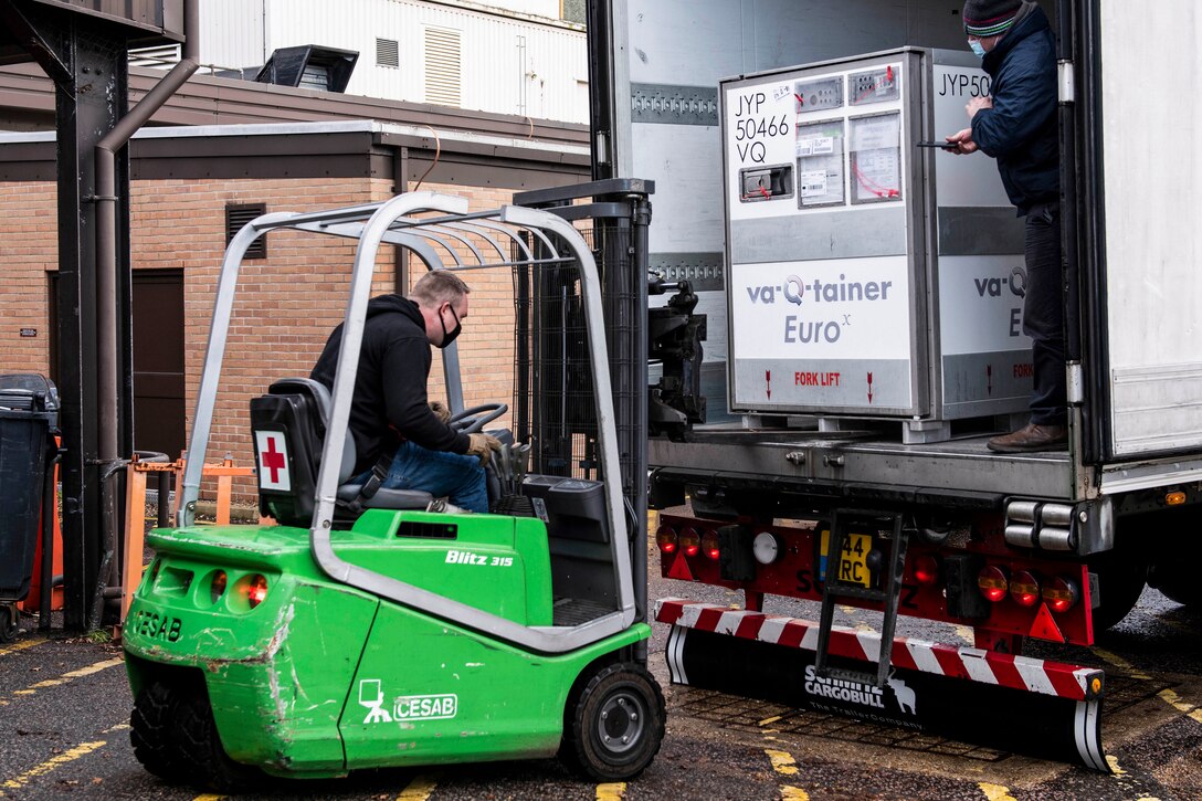 A driver positions a forklift at the back of an open truck with a large container in it.
