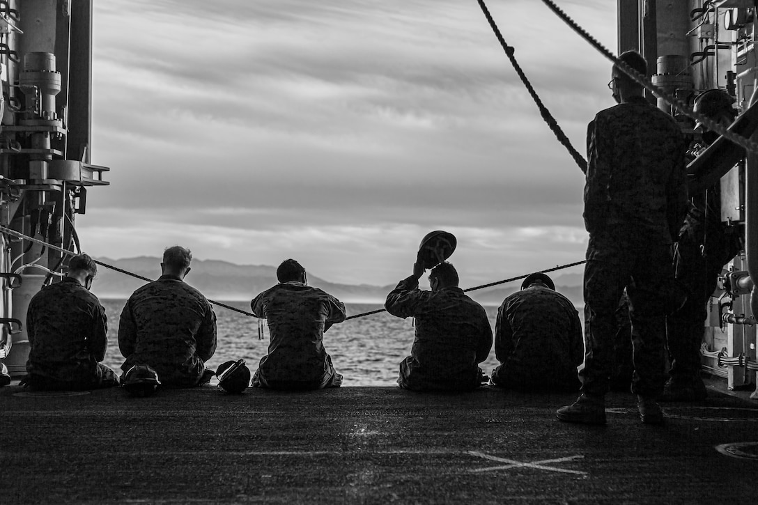 U.S. Marines with Combat Logistics Battalion 1 wait on the side of the USS Portland.