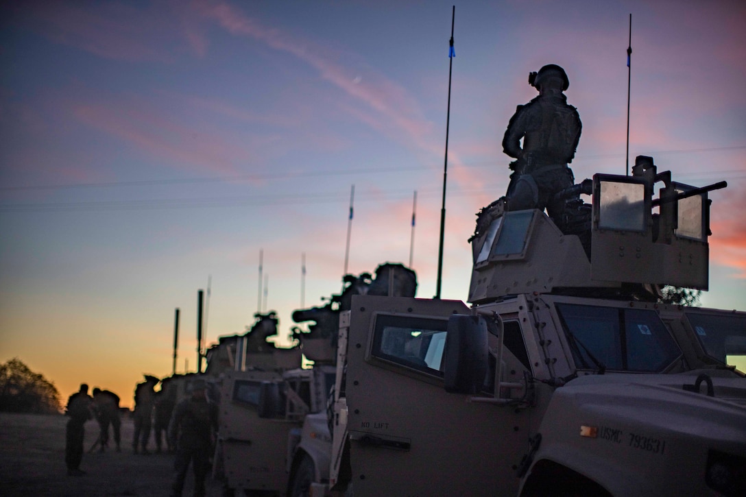 Marines stand on and around a row of military vehicles.