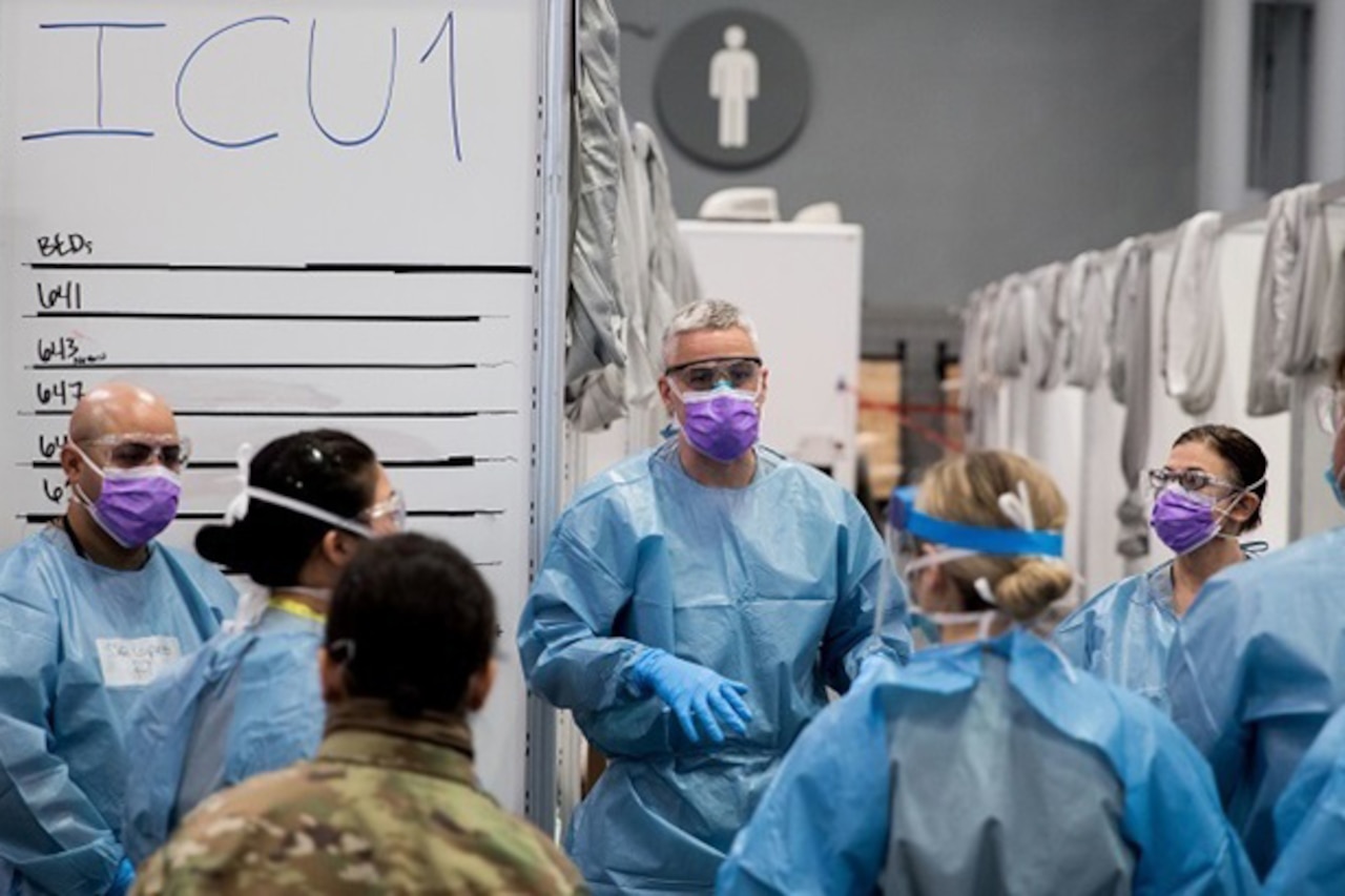 Medical students in personal protective gear listen to a man.