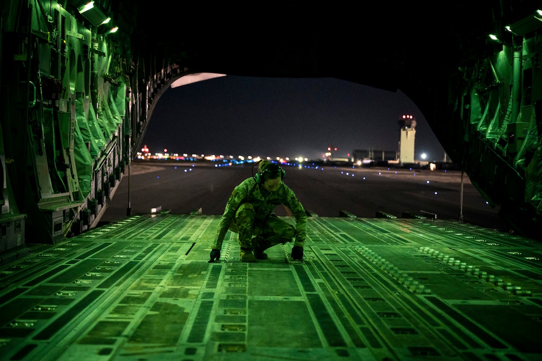 An airman kneels inside an open Globemaster illuminated by green light.