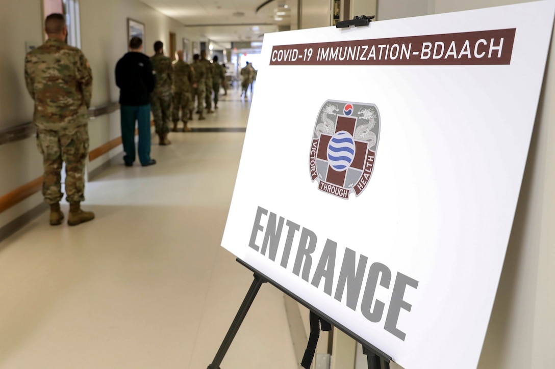 Service members stand in line in a hallway with a sign on a stand displayed in the foreground.