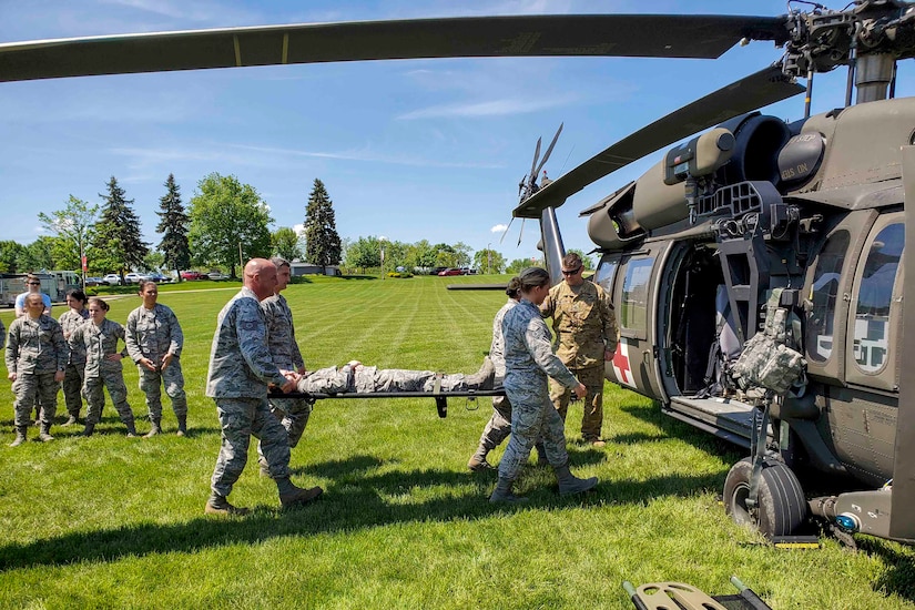 Airmen put a person on a stretcher into a waiting helicopter in a field.