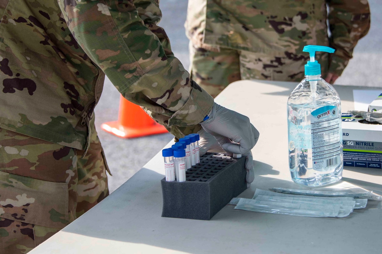 A person with gloved hands puts a vial into a secure container on a table.