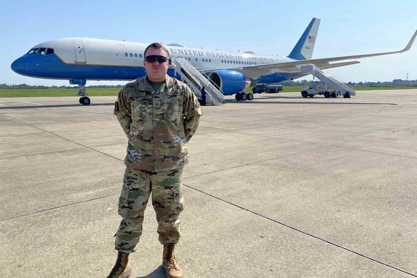 An airman stands on the tarmac in front of a passenger jet.