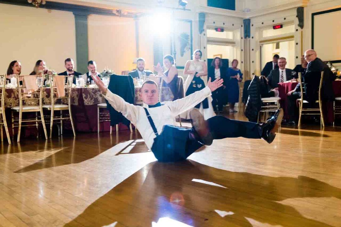 A man sits with his arms and legs up in the air on a dance floor.