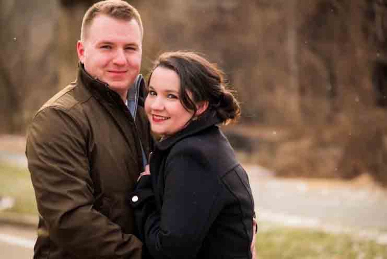 A couple in winter jackets huddles together outside.