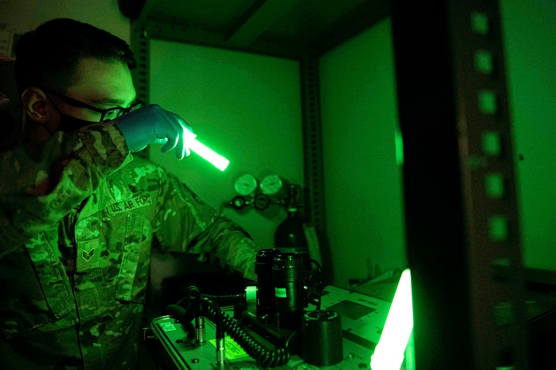 An airman looks at googles in a room illuminated by green light.