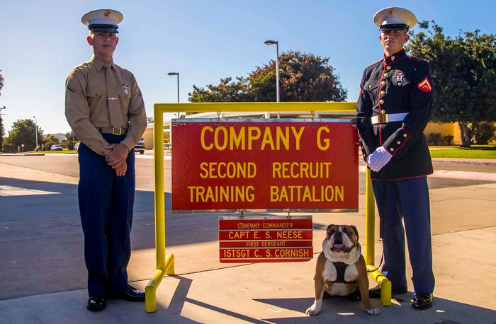 Pfc. Daniel Graven (left) and Lance Cpl. Stephen Graven (right), Marines of Golf Company, 2nd Recruit Training Battalion, stand outside of their squadbay with Lance Cpl. Manny, Marine Corps Recruit Depot (MCRD), San Diego, mascot at MCRD Dec. 18, 2020.