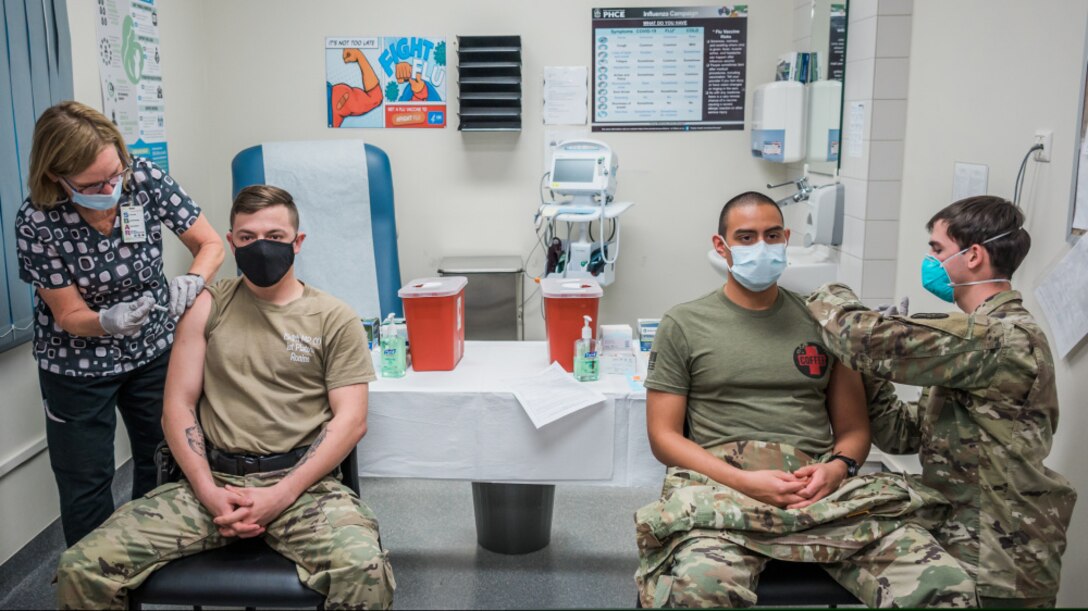 WIESBADEN, Germany – The first two COVID-19 vaccines at the Wiesbaden Army Health Clinic were administered simultaneously to Sgt. Hunter Gonzales (left), military police, and Sgt. Luis Pineda (right), NCO of the Soldier Ready Medical Center, by nurses Julia Crissinger and Sgt. Eron Johnson Dec. 30, 2020. First responders and medical personnel from the Wiesbaden Army Health Clinic were the first to receive the vaccine in this initial phase of the distribution. Photo/caption by Lisa Bishop, U.S. Army Garrison Wiesbaden public affairs.
