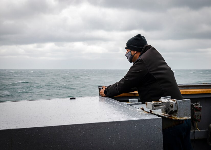 A sailor stands on the bridge wing of a ship and scans the horizon.