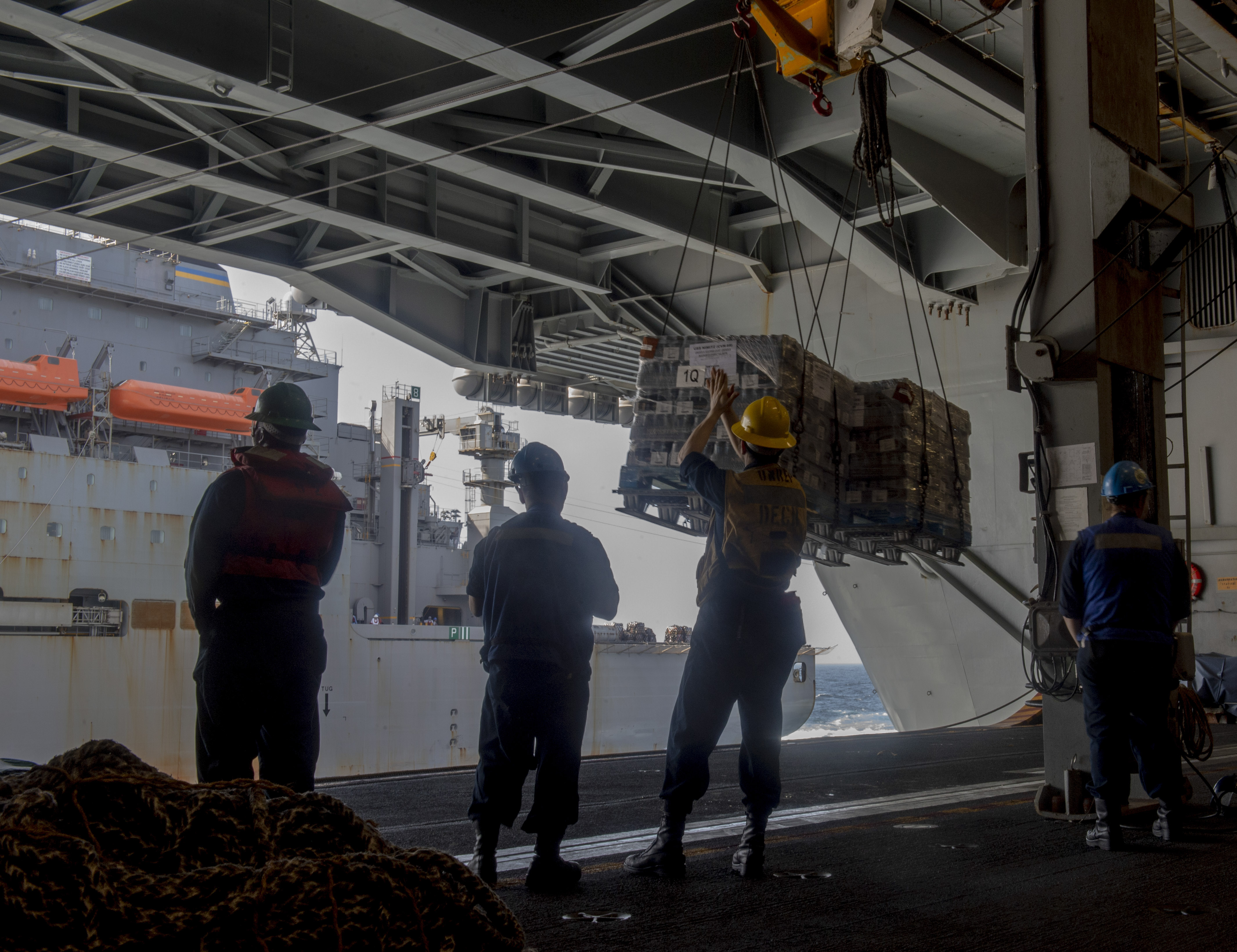 Sailors receive cargo in the hangar bay of the aircraft carrier USS Nimitz (CVN 68) during a replenishment-at-sea with the Lewis and Clark-class dry cargo ship USNS Carl Brashear (T-AKE 7).