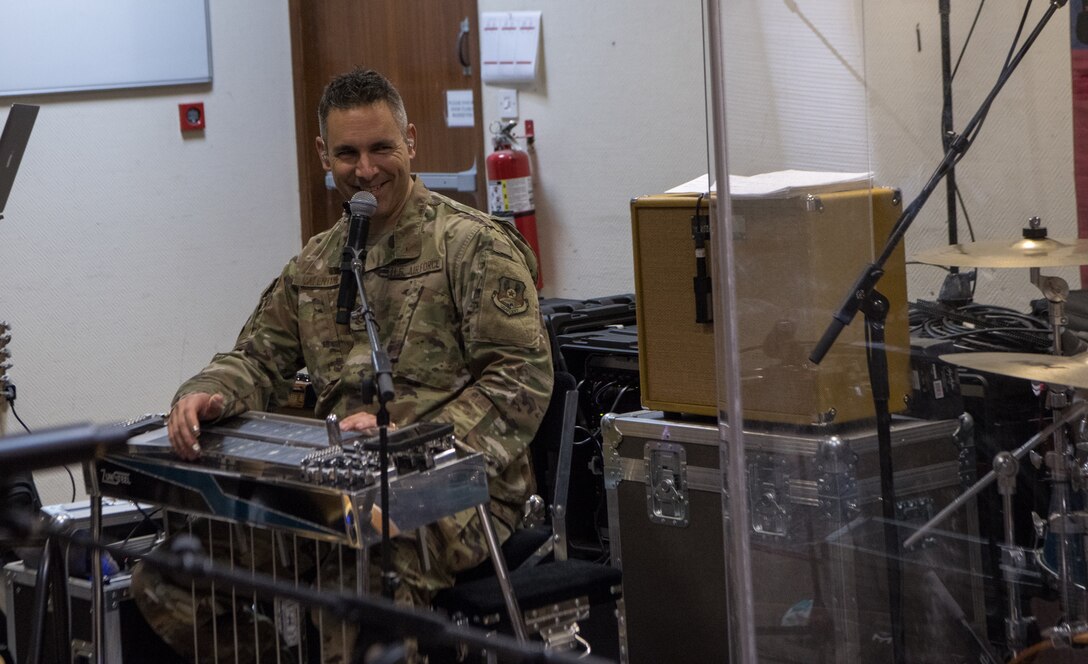 man sitting behind steel guitar smiles into microphone