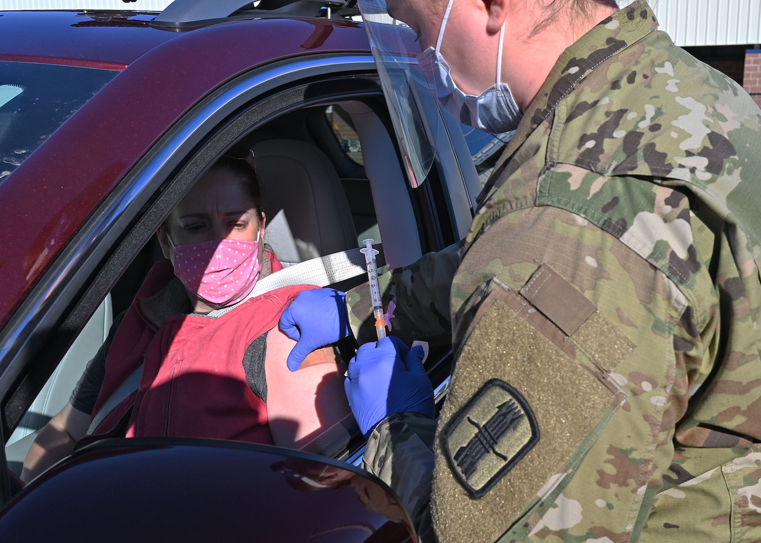 Spc. Madalyn Stella, combat medic, 197th Field Artillery Brigade, NHARNG, applies a bandage after vaccinating Stacy Gillis, a civilian paramedic, Dec. 29 in Exeter, N.H