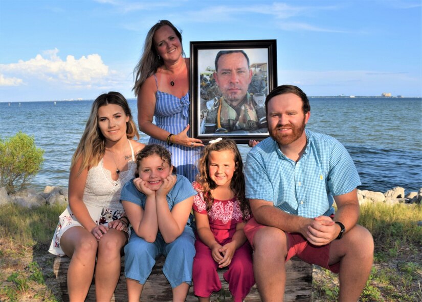 Sarah Smith holds a framed photograph of her late husband, Sgt. 1st Class James Smith during a beachfront family photo this year. Smith took part in the 94th Training Force Sustainment Headquarters and Headquarters Company virtual suicide prevention training, where she shared her story about the loss of her husband due to suicide. The 94th TD-FS HHC suicide prevention training was conducted on October 24, 2020. (Photo courtesy of Sarah Smith, widow of service member)