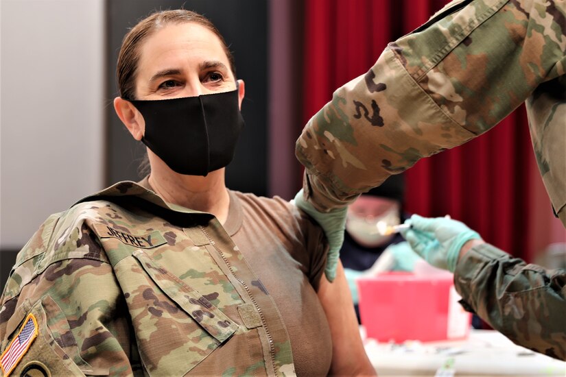 A soldier wearing a protective face mask gets a shot in the arm.