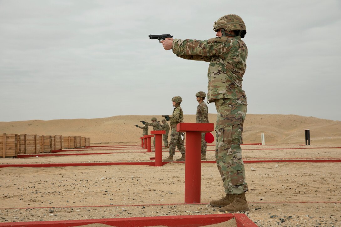 Soldiers line up and fire weapons in a desert-like area.