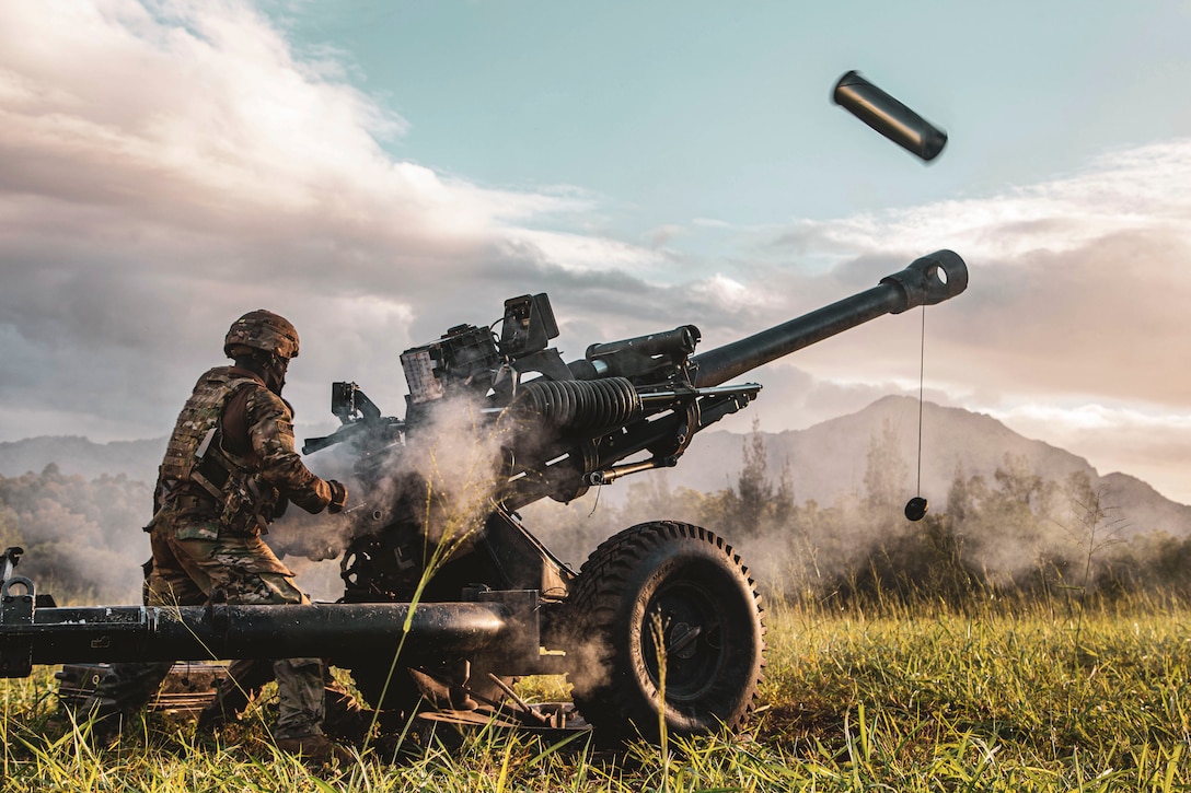 Service members fire a weapon in a field.