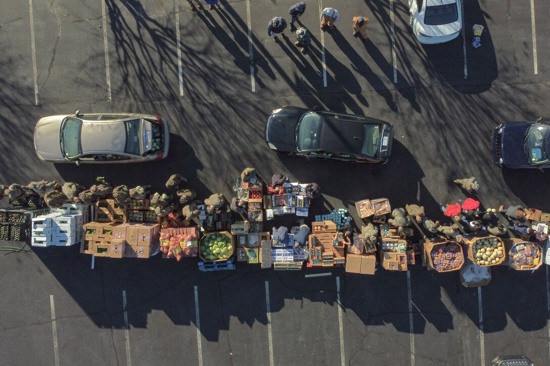 A line of cars, seen from overhead, are alongside a line of boxes filled with food in parking lot, where Marines and other volunteers work.