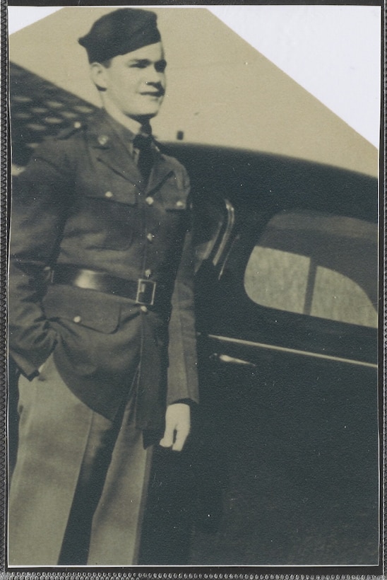 A man in a military uniform stands in front of a vehicle.