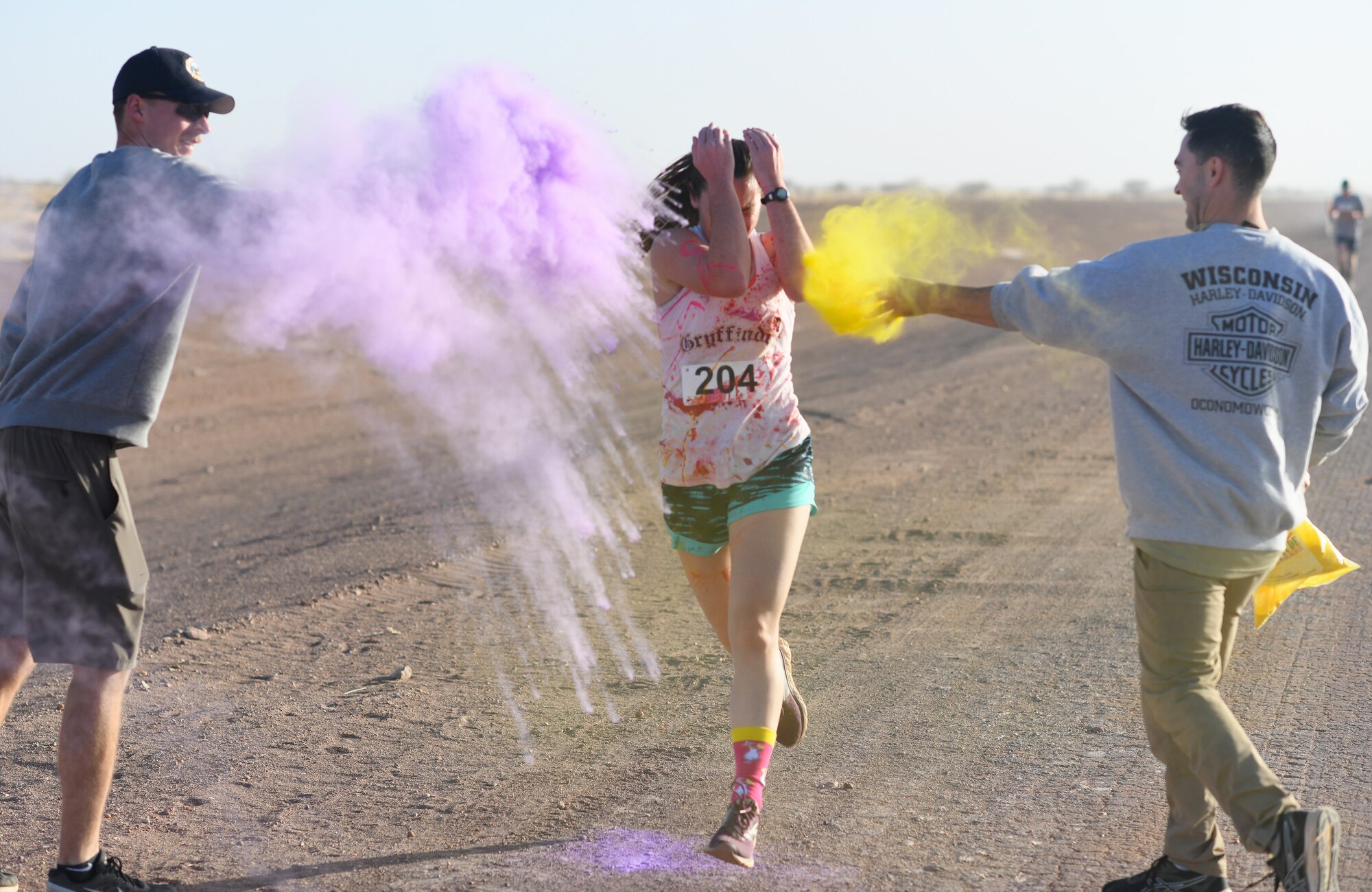 A color run participant runs through a gauntlet of paint throwing volunteers at Nigerien Air Base 201, Niger, Feb. 2, 2020. More than 30 runners and volunteers participated in the event. (U.S. Air Force photo by Tech. Sgt. Alex Fox Echols III)