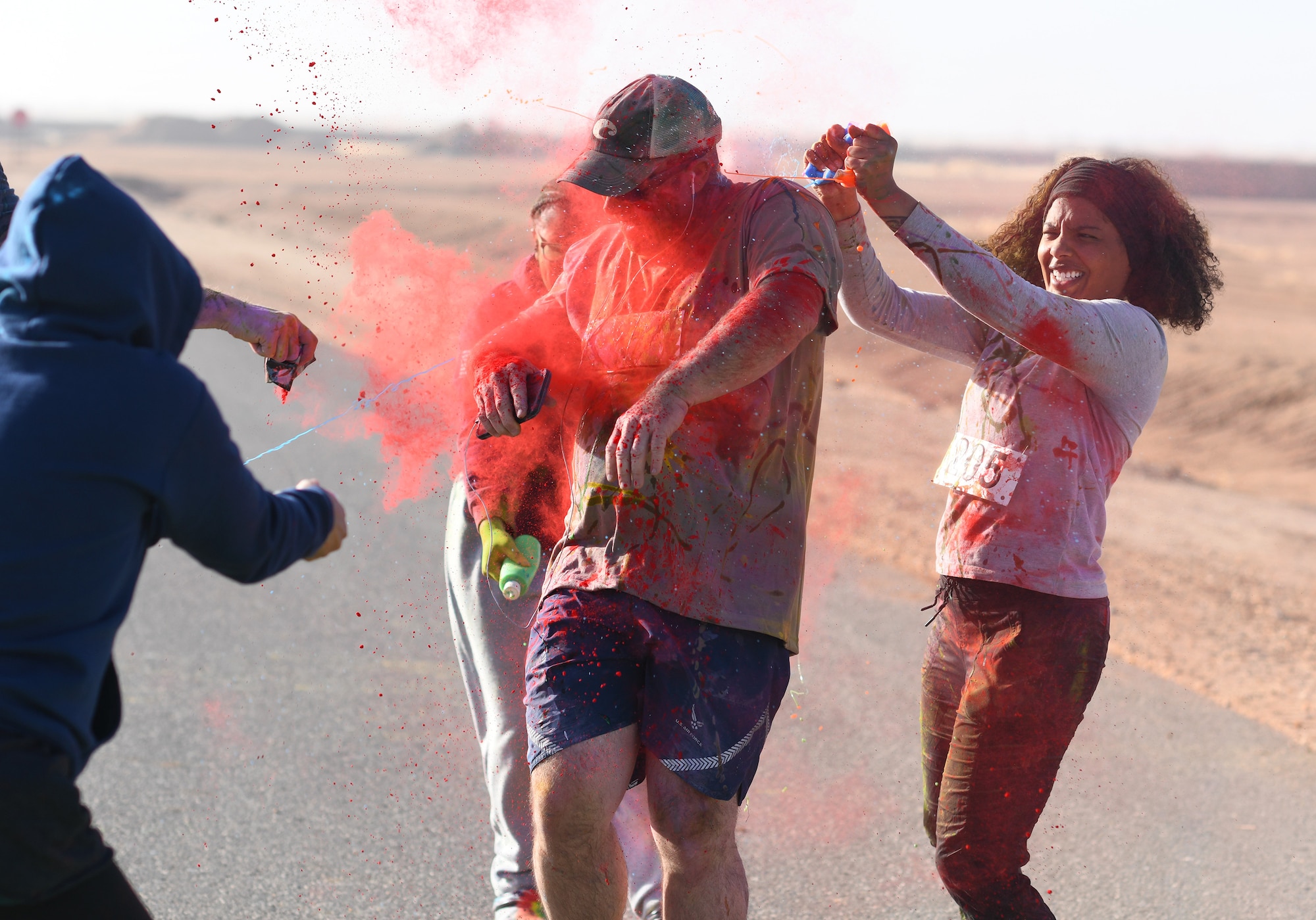 A color run participant runs through a gauntlet of paint throwing volunteers at Nigerien Air Base 201, Niger, Feb. 2, 2020. More than 30 runners and volunteers participated in the event. (U.S. Air Force photo by Tech. Sgt. Alex Fox Echols III)