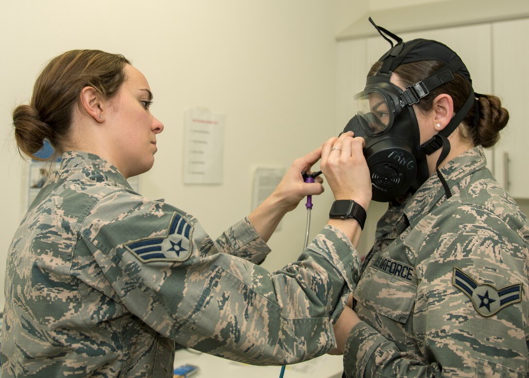 An airman puts a gas mask on another airman.