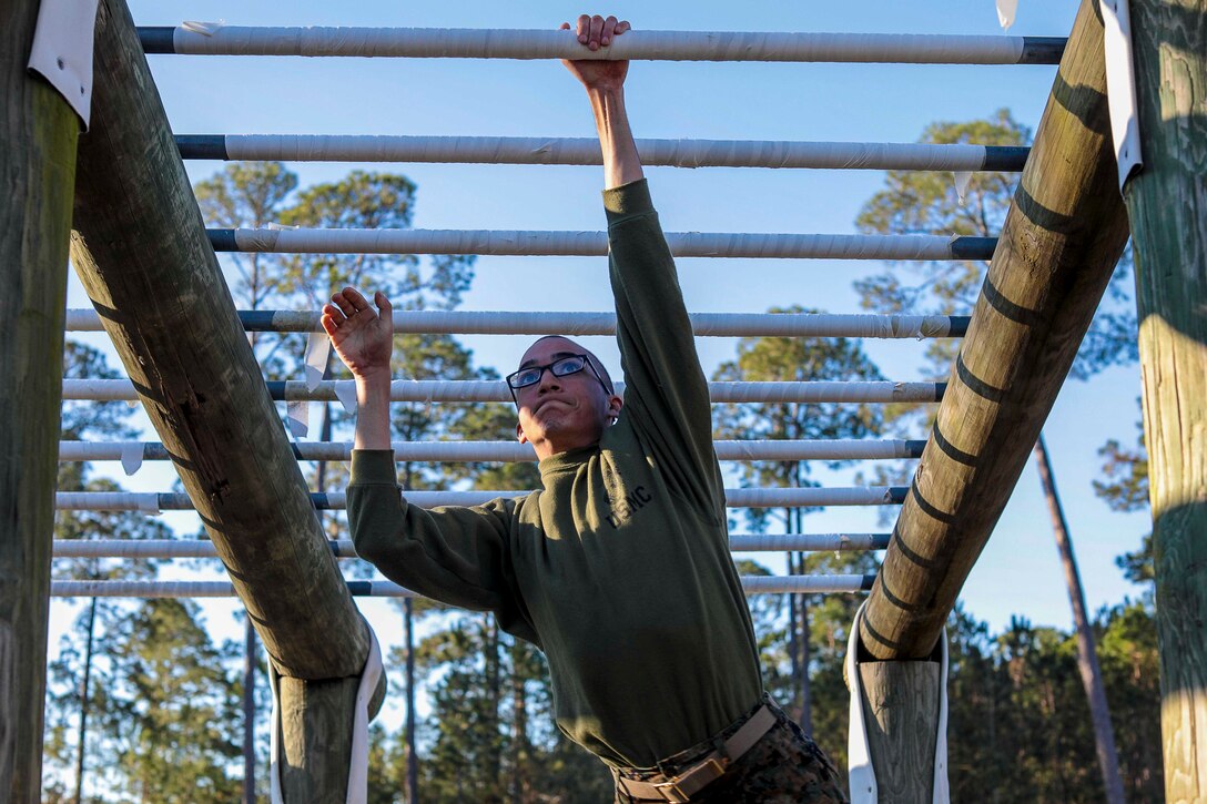 A Marine Corps recruit moves through a horizontal ladder obstacle.