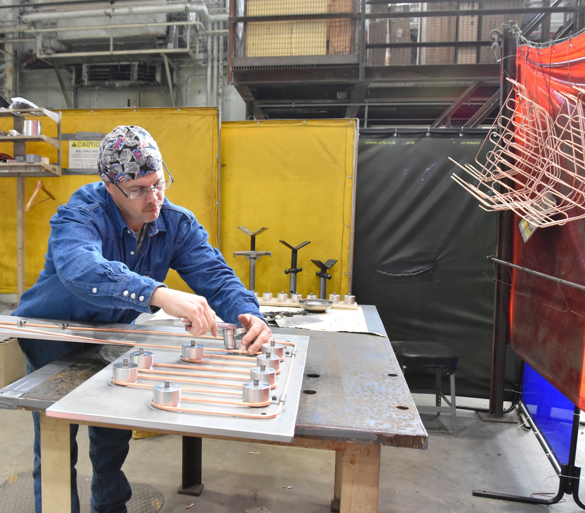 Darrell Hargrove, a pipefitter in the Model and Machine Shop at Arnold Air Force Base, uses a jig to bend copper tubing to fit within tape reel covers that will be installed in the 16-foot supersonic wind tunnel, known as 16S, at Arnold. Completed bends are shown hanging on the right. This is among numerous efforts undertaken by craftsmen at Arnold which have contributed to the 16S return to service project. (U.S. Air Force photo by Bradley Hicks)