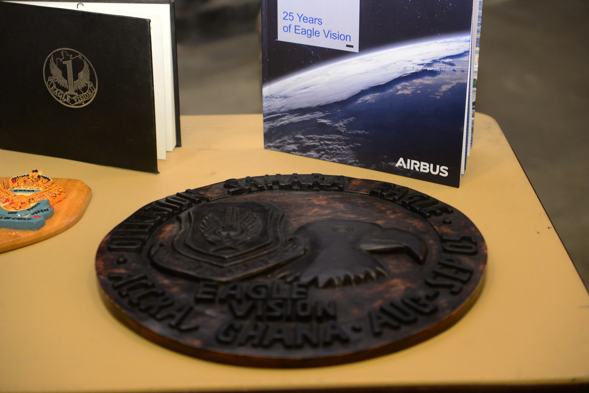 A wooden plaque, memorializing Eagle Vision One in Ghana, lays on a table during a sunset ceremony at Ramstein Air Base, Germany, Jan. 28, 2020. Eagle Vision One used satellite imagery to support operations as well as aiding allies during natural disasters. (U.S. Air Force photo by Airman 1st Class Manuel Zamora)