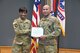 Female Soldier in green camouflage uniform holds green folder with white certificate with male Soldier in green camouflage uniform in front of the U.S. flag and the Army and Recruiting Command colors all of which are red, white and blue.