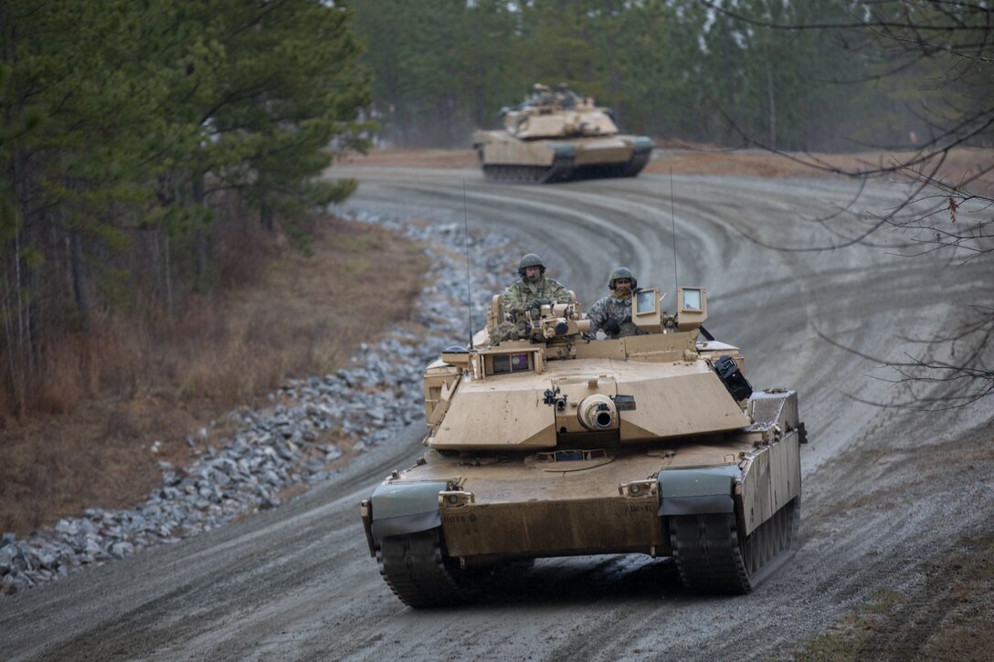 A soldier drives a tank as another one follows behind.