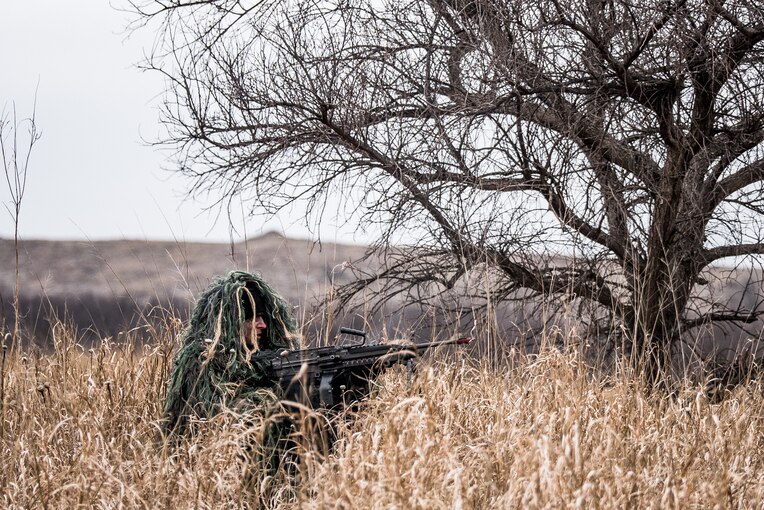 A soldier ducks in tall grass while holding a weapon.