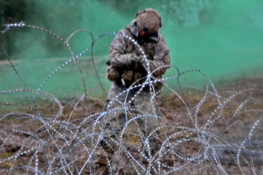 A soldier pulls a wire in a field surrounded by green smoke.