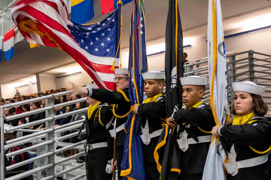 A group of Navy recruits in formation hold flags.