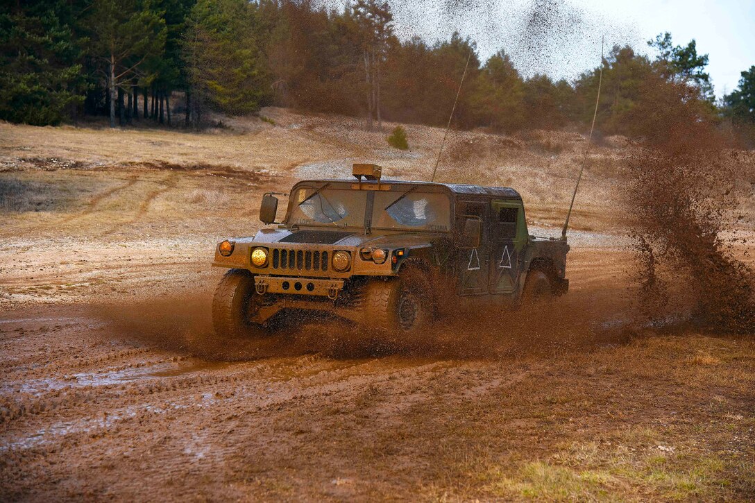 A military vehicle drives through mud.