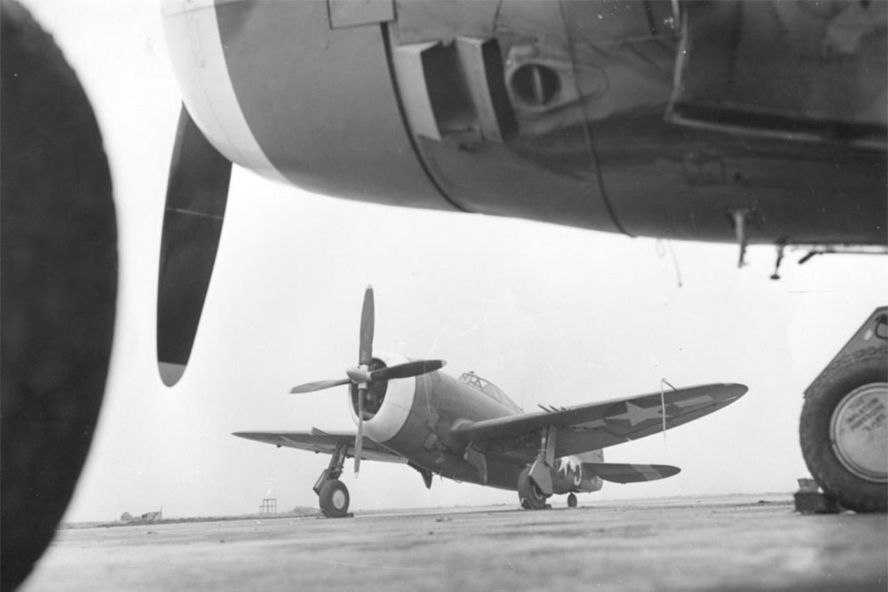 Two propeller airplanes sit on an airstrip. One is fully seen in the background; only the front and one propeller blade of the second can be seen in the foreground.