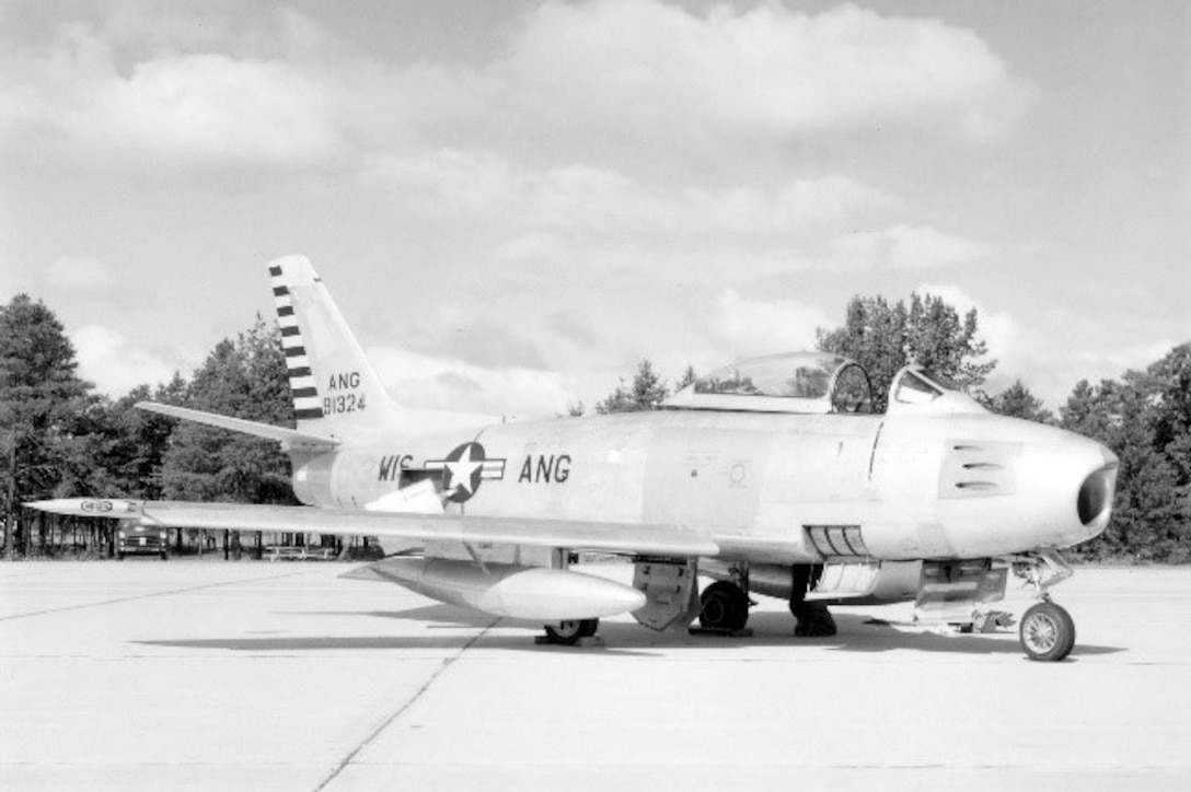 A F-86A Sabre fighter jet sits on an air strip as trees can be seen in the background.