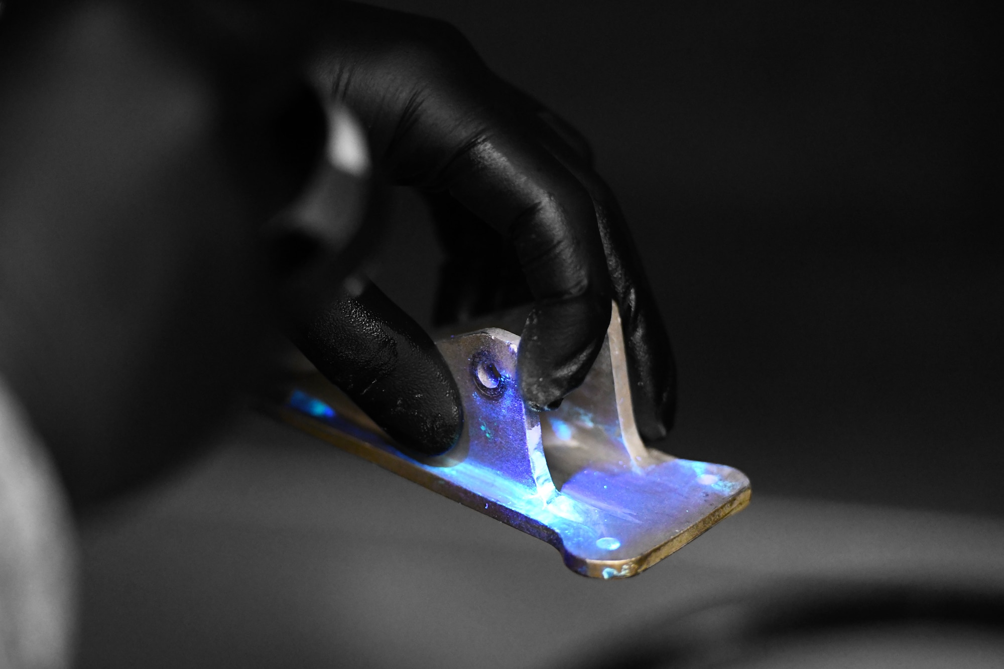 Airman 1st Class Camden Roman, 100th Maintenance Squadron non-destructive inspection journeyman, shines an ultraviolet light on a part at RAF Mildenhall, England, Jan. 23, 2020. The NDI shop helps ensure aircraft safety by using florescent penetrants among other methods to detect cracks in aircraft parts that may be invisible to the naked eye.(U.S. Air Force photo illustration by Staff Sgt. Lexie West)