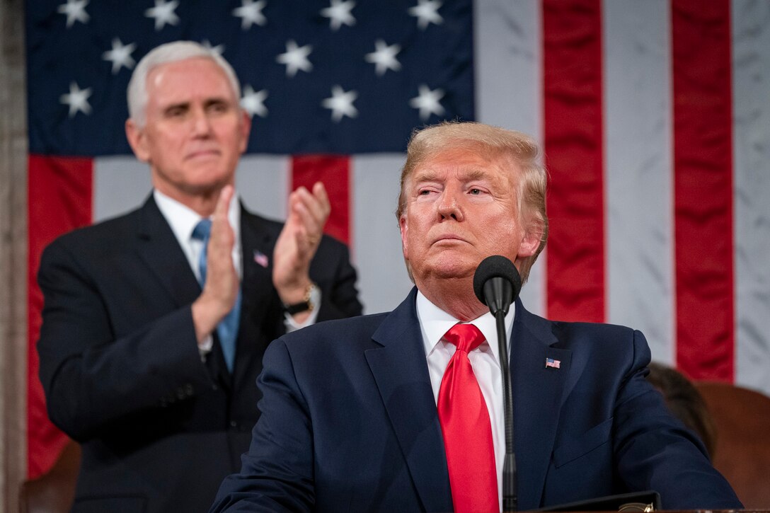 President Trump pauses during speech, with vice president standing and applauding in background.