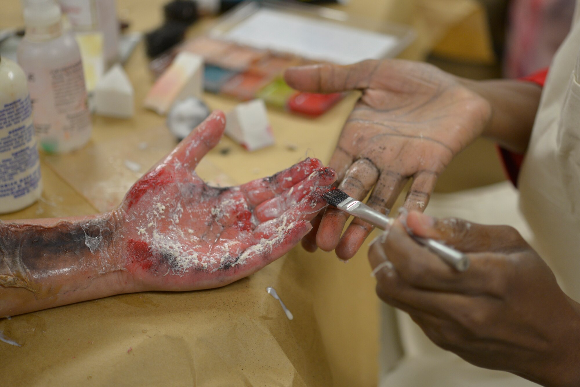 U.S. Air Force Staff Sgt. Crystal Abad, 81st MDG internal medicine technician, has moulage applied on her hand by Sharon Simmons, 81st Medical Group internal medicine licensed practical nurse, inside Wolfe Hall at Keesler Air Force Base, Mississippi, Jan. 29, 2020. Moulage, also known as combat injury simulation, is used in base exercises to simulate the outcome of various situations such as chemical burns, piercing wounds and missing limbs using different tools such as latex, stage blood, sponges and makeup products. (U.S. Air Force photo by Airman 1st Class Kimberly Mueller)